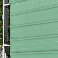 Downspout installed on a green metal building by Gutter Haven