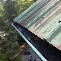 Debris-filled gutter on a metal roof cleaned out by Gutter Haven